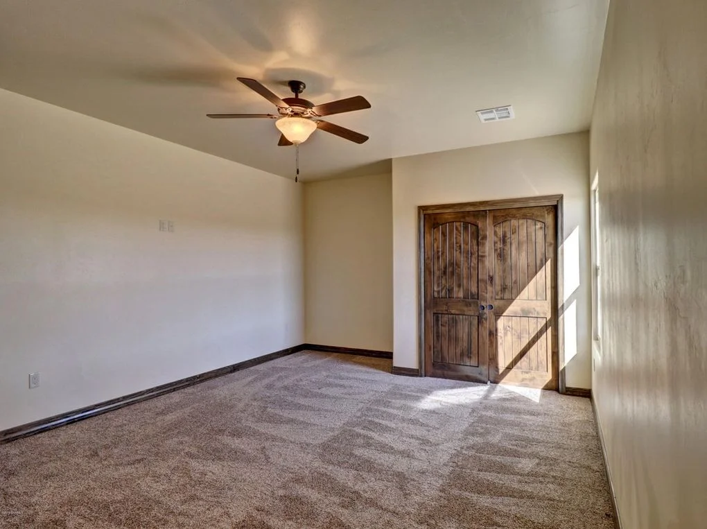 Finished bedroom with gray carpet, cream walls, wood closet doors, and ceiling fan