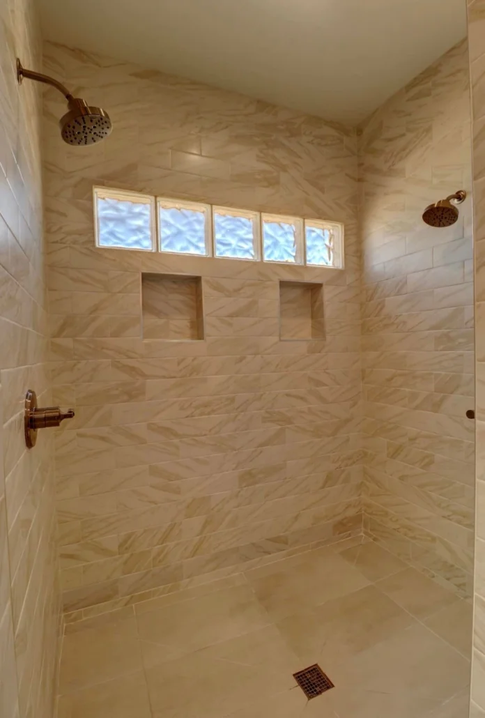 Marble tile shower with dual rainfall heads, recessed shelving, and transom windows