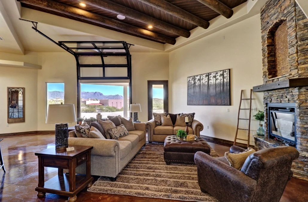 Living room with exposed wood beams, stone fireplace, glass garage door, and polished concrete floors