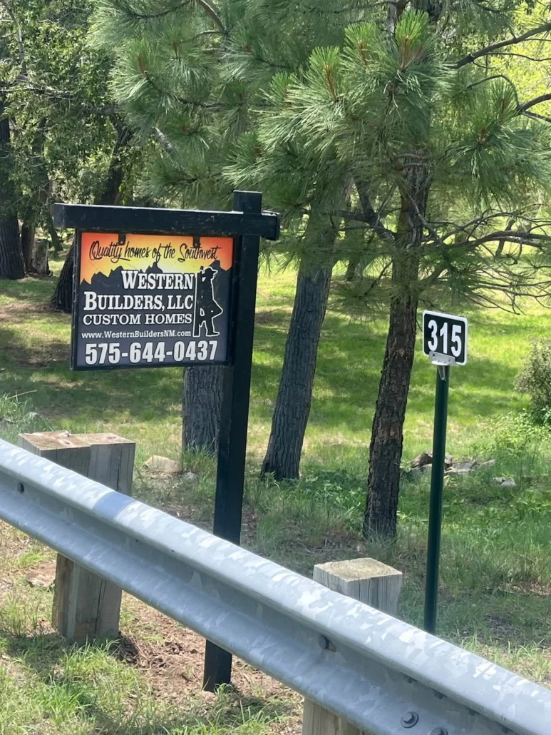 Metal guardrail and driveway entrance with custom home builder signage at wooded residential site