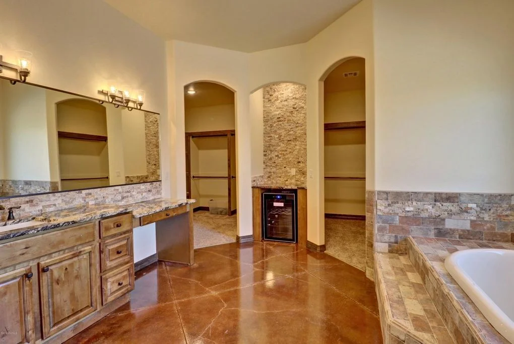 Master bathroom with travertine tile, polished concrete floors, wood cabinetry, and arched alcoves