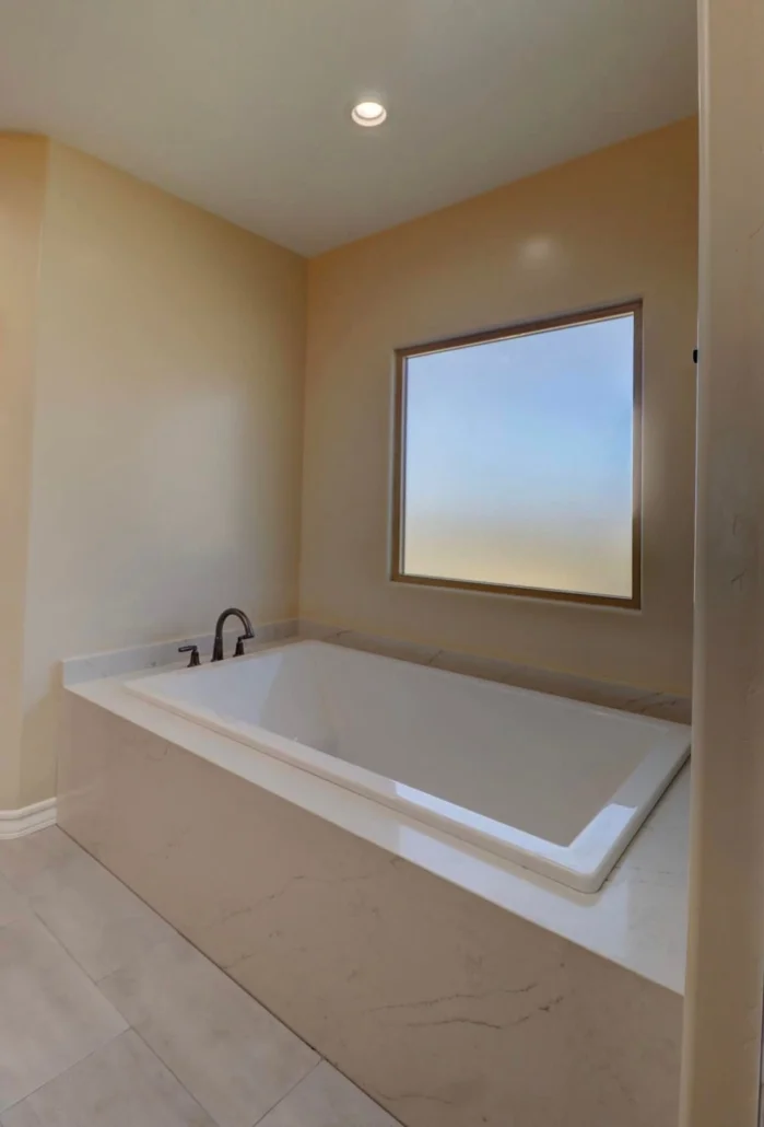 Master bathroom with white soaking tub, beige walls, recessed lighting, and picture window