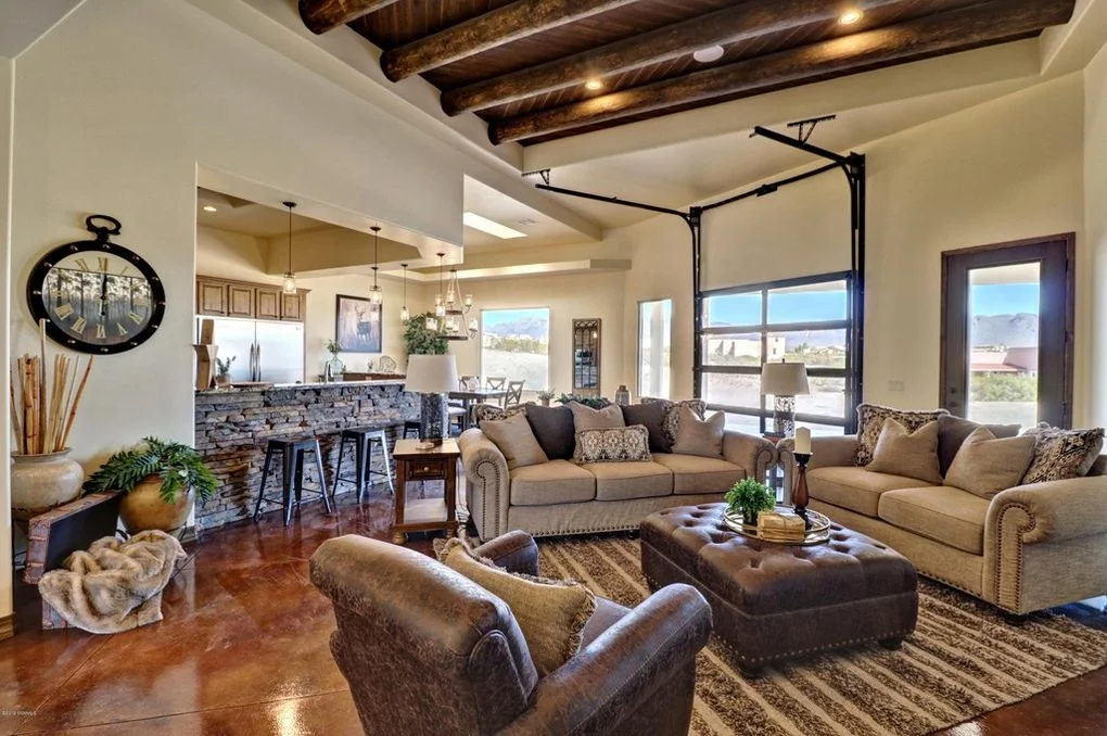 Open living area with exposed wood beams, stone accent wall, polished concrete floors, and large windows
