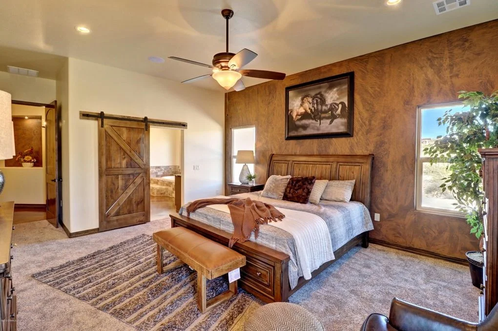 Master bedroom with textured walls, wood barn doors, ceiling fan, and wood bed frame