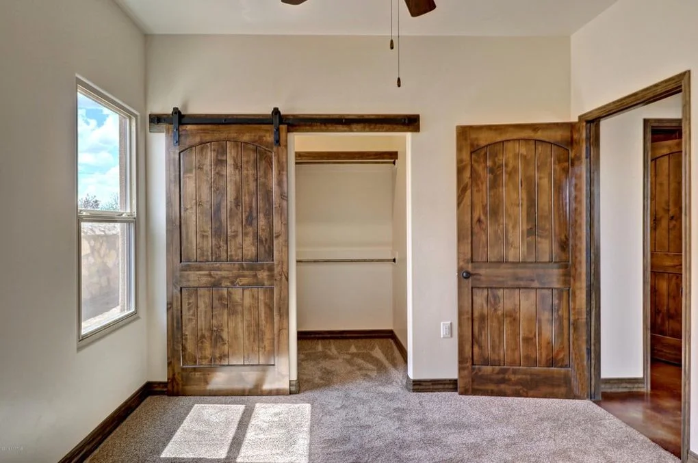 Rustic arched barn doors with iron hardware flanking walk-in closet in bedroom