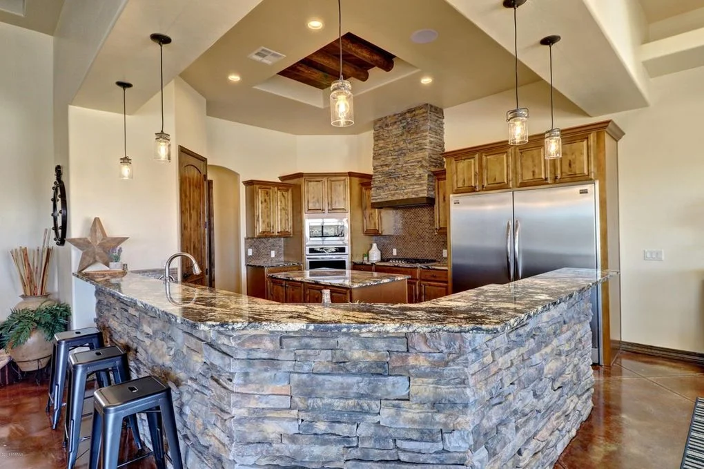 Stone veneer kitchen island with granite top, wood cabinetry, and pendant lights