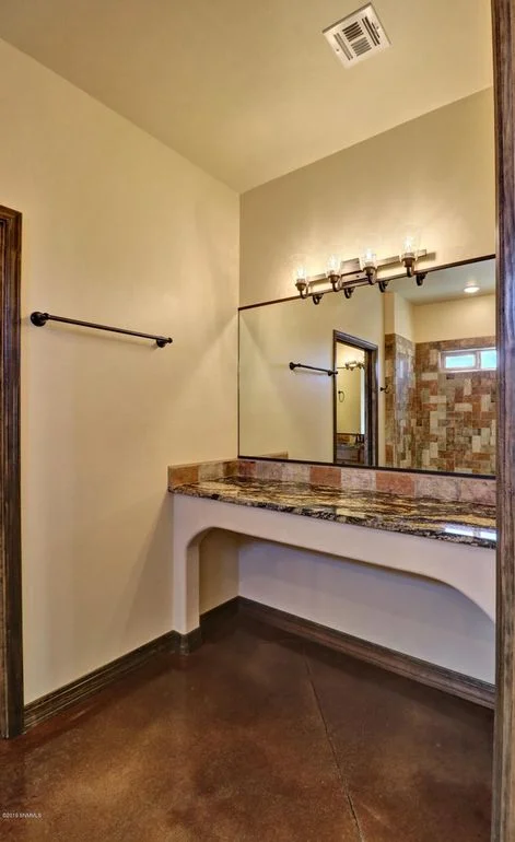 Granite vanity with framed mirror, black fixtures, and polished concrete flooring in bathroom