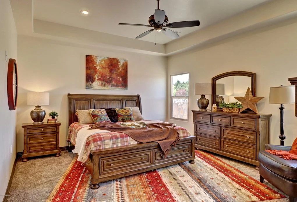 Master bedroom with wood bed frame, dresser, nightstands, tray ceiling, and ceiling fan
