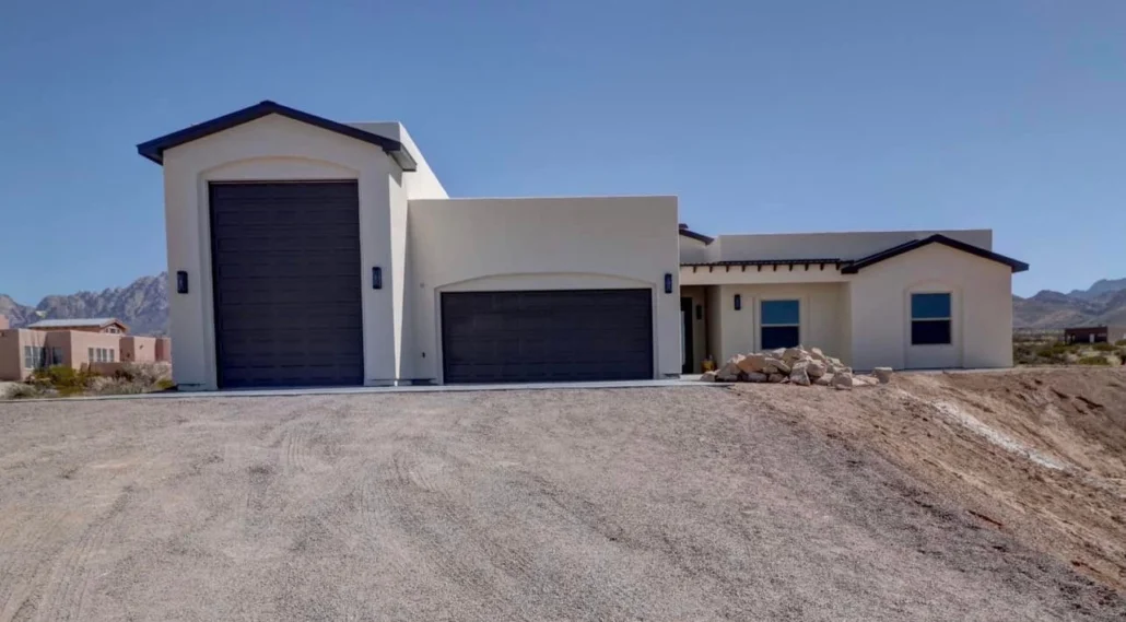 White stucco home with dark garage doors, modern architectural design, desert landscape setting