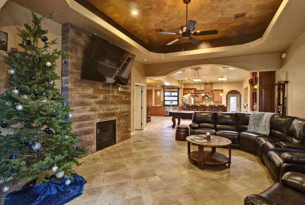 Family room with bronze coffered ceiling, stacked stone fireplace, tile flooring, and black leather seating