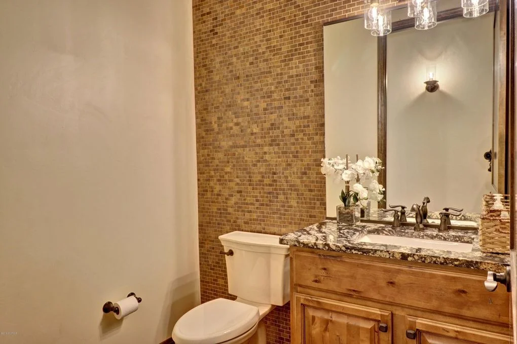 Bathroom with granite countertop, wood vanity, brick tile accent wall, and framed mirror