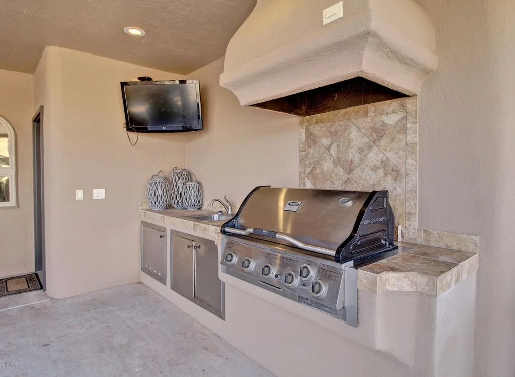 Built-in stainless steel grill with stone tile backsplash and white hood vent in outdoor kitchen
