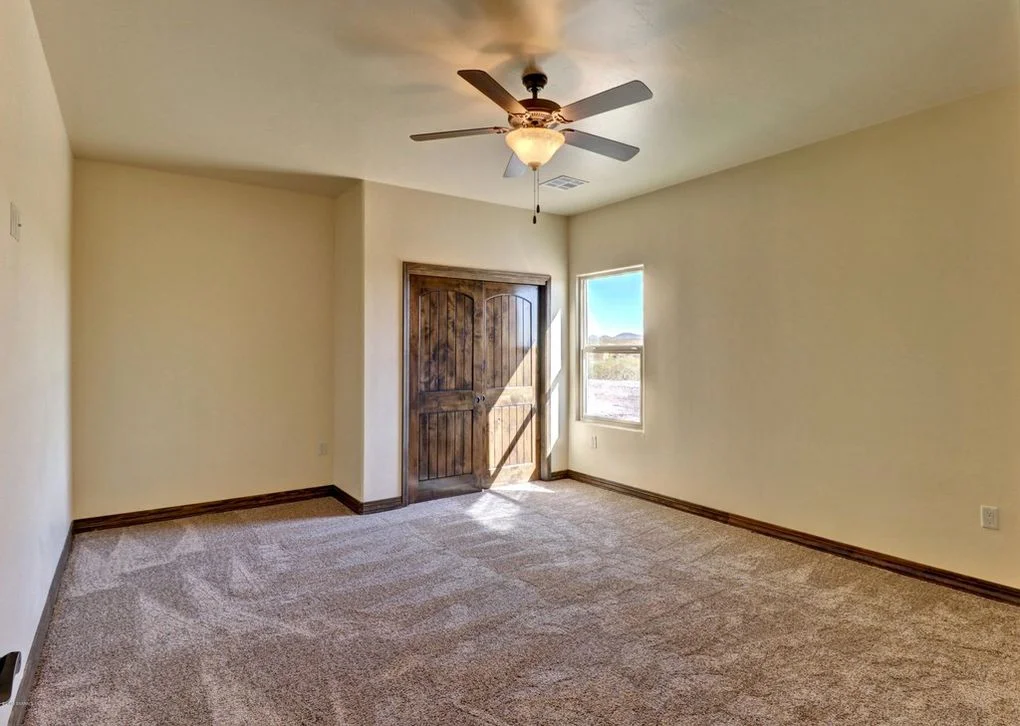 Spacious bedroom with beige walls, dark wood trim, carpet flooring, and ceiling fan with light fixture
