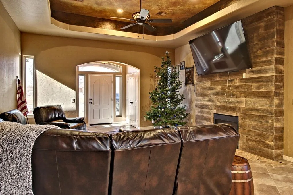 Custom family room with stacked stone fireplace, coffered tray ceiling, and leather seating