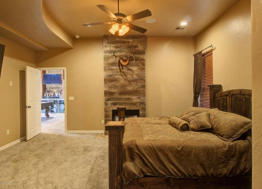 Master bedroom with stacked stone fireplace wall, ceiling fan, and wood bed frame