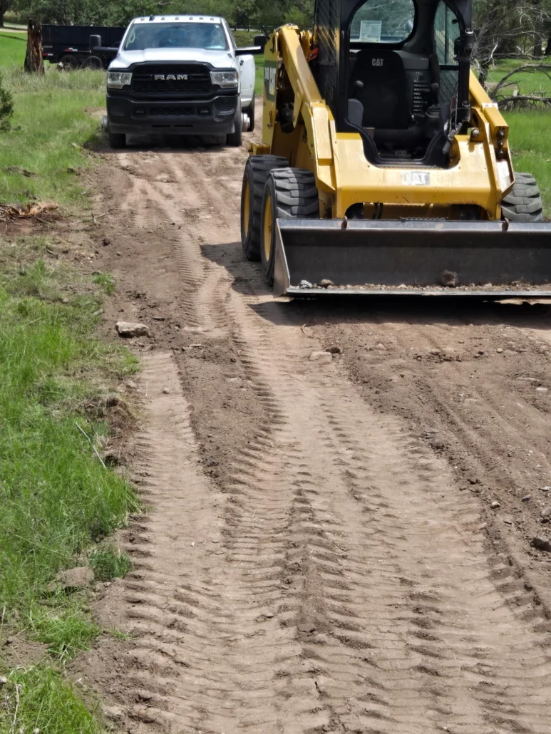 CAT skid steer with blade grading dirt driveway, cleared vegetation on sides