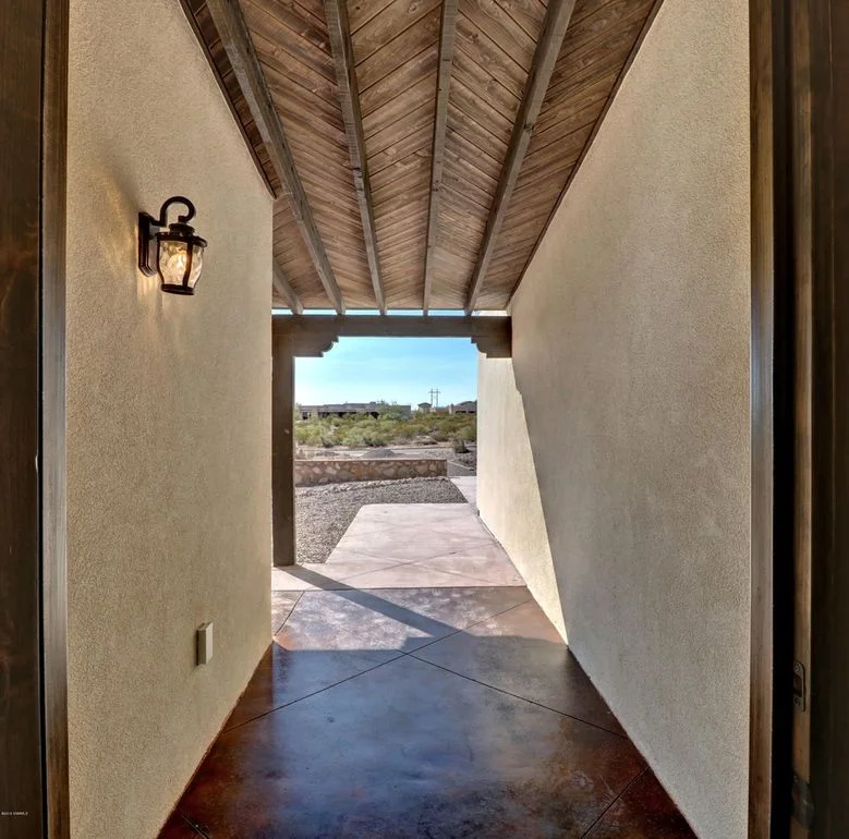Stucco entry corridor with wood beam ceiling, polished concrete floor, and desert landscape view