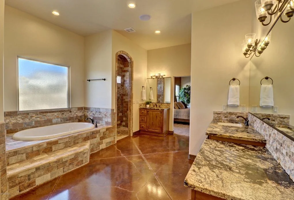 Master bathroom with stone tub surround, granite vanities, and polished concrete floors
