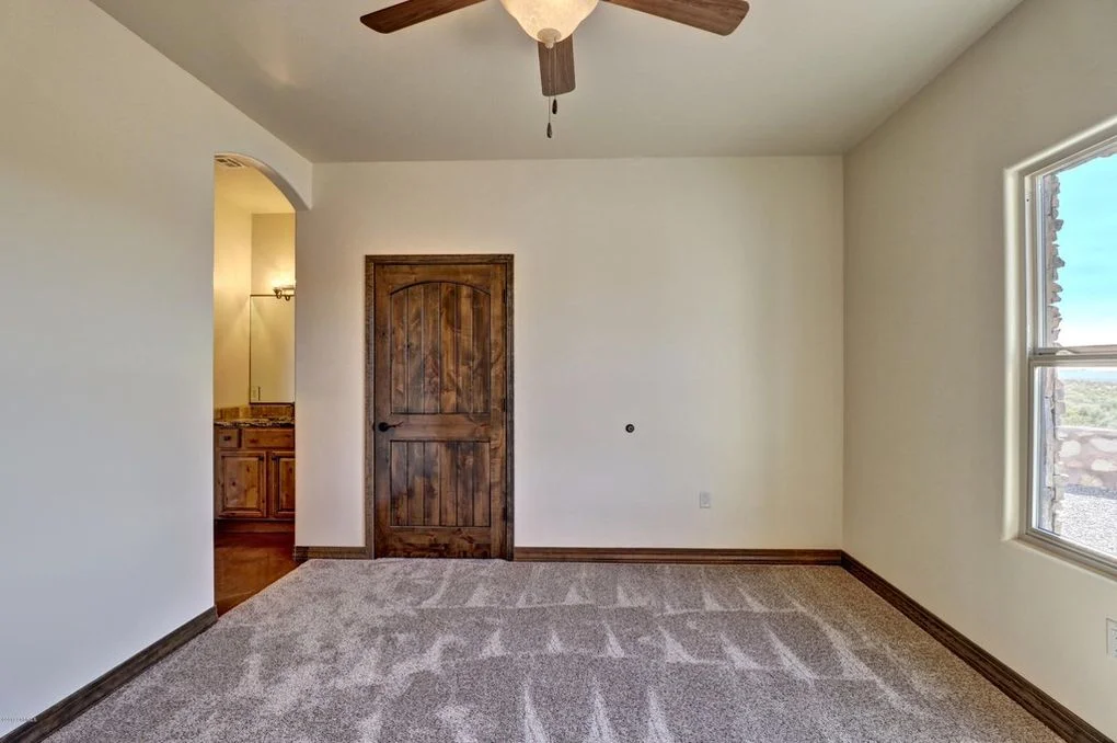 Bedroom with gray patterned carpet, white walls, wood door, and ceiling fan