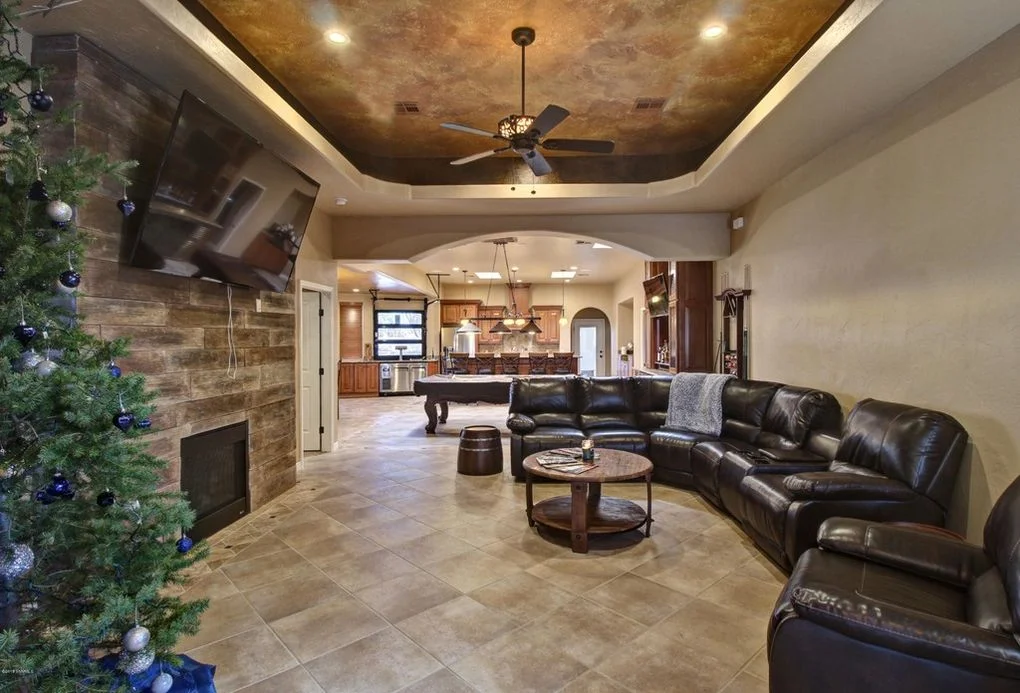 Family room with metallic tray ceiling, stone fireplace, tile flooring, and leather seating
