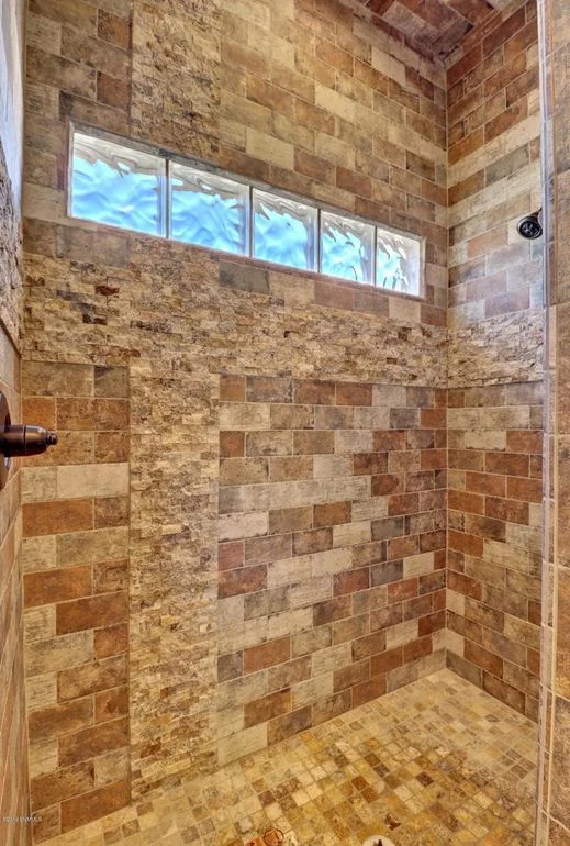 Natural stone tile shower with running bond pattern, transom windows, and bronze fixtures