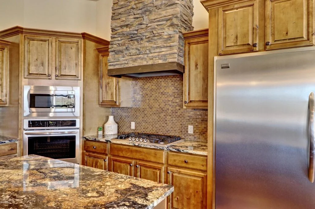 Kitchen with knotty alder cabinets, granite counters, stacked stone chimney, and stainless steel appliances