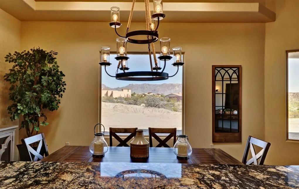 Dining room with granite island, black chandelier, and desert mountain view through large window