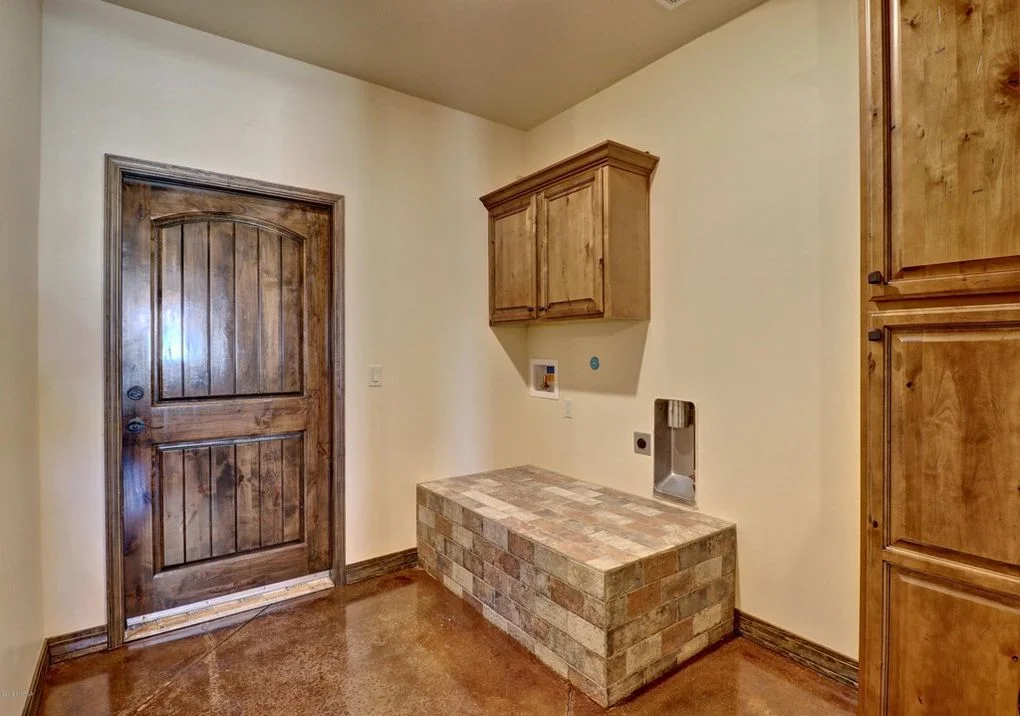 Utility room with stacked stone island, wood cabinetry, concrete flooring, and rustic doors