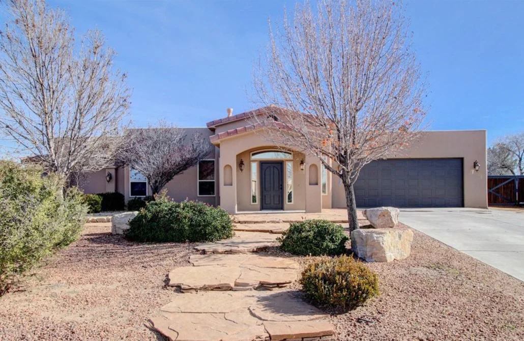 Stucco home with curved portico entry, arched door, two-car garage, and desert landscaping