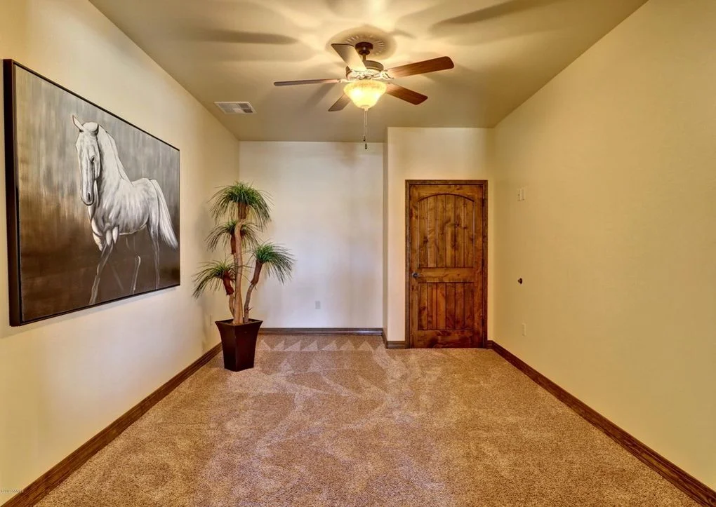 Finished guest bedroom with yellow walls, carpet flooring, wood door, and ceiling fan