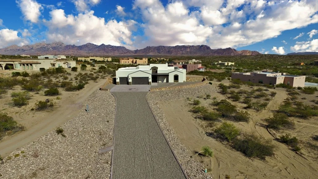 Aerial view of completed asphalt driveway with gravel borders and French drain system leading to modern home
