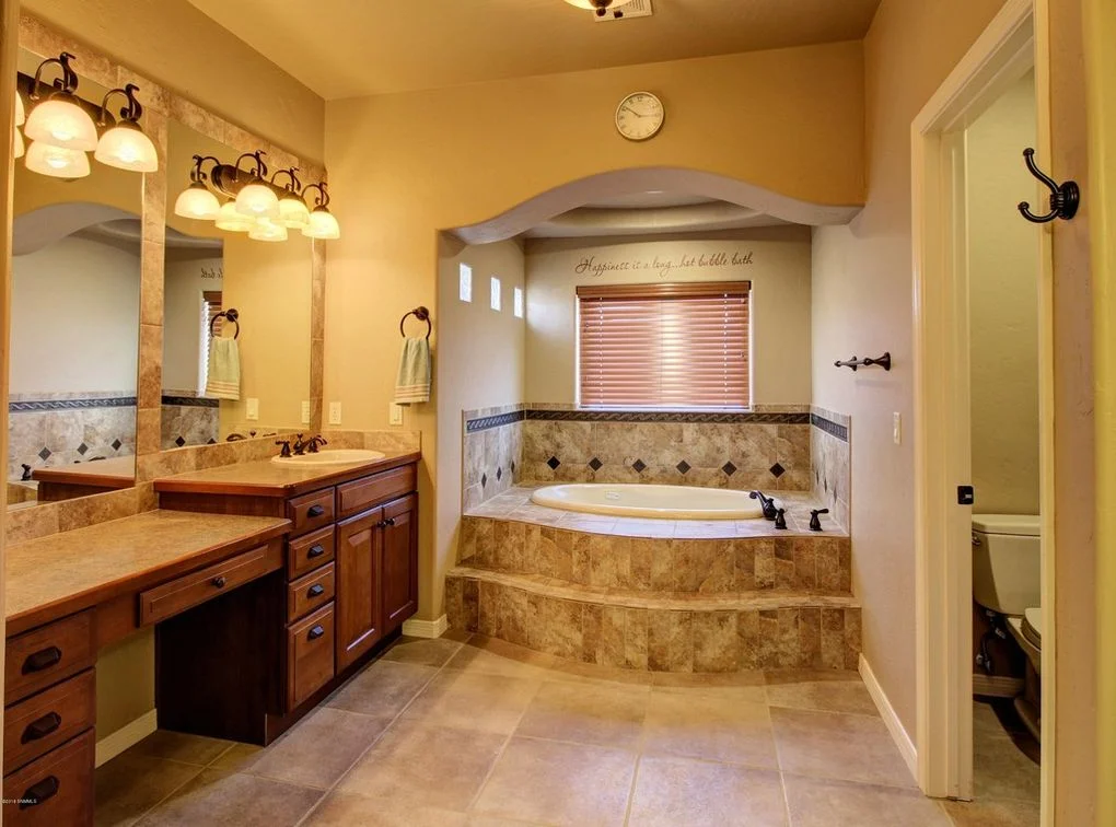 Master bathroom with travertine tile, granite counters, soaking tub, and double vanity